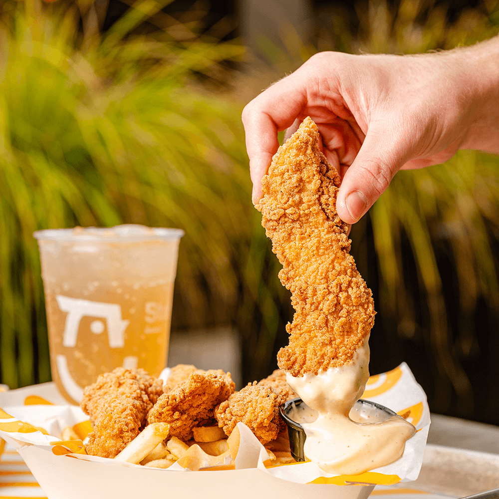 Hand dipping a Starbird Chicken strip into a cup of sauce